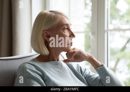 Nachdenkliche reife Frau sieht im Ferndenken zuhause aus Stockfoto