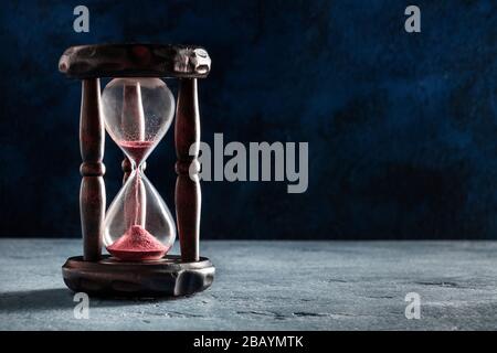 Das Konzept der Zeit läuft aus. Eine Sanduhr mit durchfallendem Sand, auf dunklem Hintergrund mit Textstelle Stockfoto