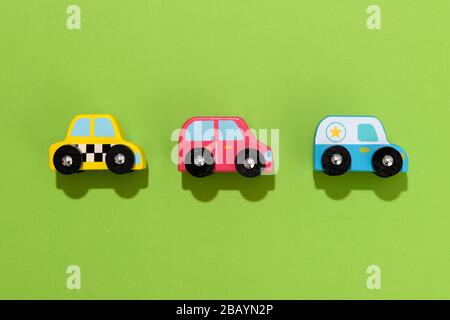 Drei bunte Holzspielzeugautos auf grünem Hintergrund, die sauber in einer Reihe in der Mitte mit Schlagschatten und Kopierräumen platziert sind Stockfoto
