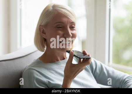 Lächelnde Frauen mittleren Alters verwenden Sprachassistenten auf dem Smartphone Stockfoto