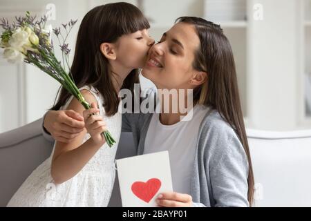 Kleine Tochter gratuliert aufgeregter junger Mutter, die Blumen präsentiert Stockfoto