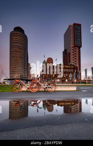 Rotterdam - 12. Februar 2019: Rotterdam, Niederlande. Hotel New York. Zwei rote Fahrräder, die vor dem Hotel geparkt wurden, das Hotel und die Fahrräder Stockfoto