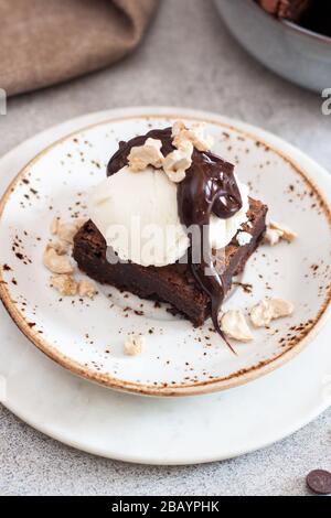 Hausgemachte Brownie mit einer Schaufel Vanilleeis, Schokoladensoße und Nüssen Stockfoto