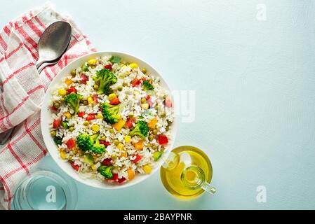 Frischer Reissalat mit gemischtem Gemüse in einer Schüssel auf blauem Tisch Stockfoto