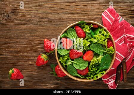 Gesunder grüner Salat mit frischem Erdbeerobst auf Holztischgrund. Gesundes Salatessen. Stockfoto