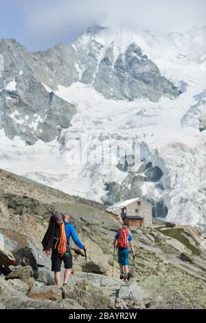 Zinal, Schweiz - 19. Juli 2019: Rückansicht von Wanderern mit Trekkking-Stöcken auf einem felsigen Pfad mit Berghängen im Hintergrund. Konzept für Reisen, Tourismus und Aktivurlaub. Stockfoto