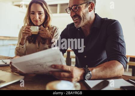 Zwei Geschäftskollegen, die am Coffee-Shop-Tisch arbeiten. Ein Geschäftsmann liest ein Dokument, während sein Kollege im Café beim Kaffeetrinken sitzt. Stockfoto