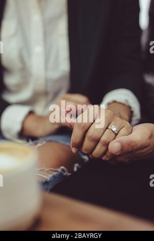 Liebevolles Paar hält die Hände in der Café-Bar zusammen. Nahaufnahme eines Mannes, der mit einem Verlobungsring die Hand seiner Frau hält. Stockfoto