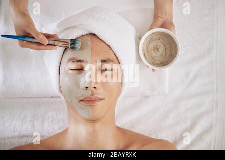 Kosmetologe, der Holzkohlemaske auf die Hälfte des Gesichts des reifen Mannes anwendet, Ansicht von oben Stockfoto