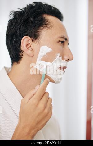 Gutaussehender Mann, der sich nach dem Duschen im Badezimmer rasiert Stockfoto