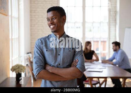 Selbstbewusster afrikanischer Geschäftsmann, der mit den Armen im modernen Sitzungssaal steht Stockfoto