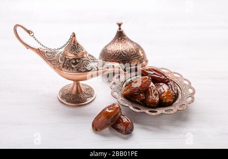 Bronzeplatte mit Datteln und aladdin-lampe auf weißem Holzhintergrund. Ramadan Hintergrund. Stockfoto