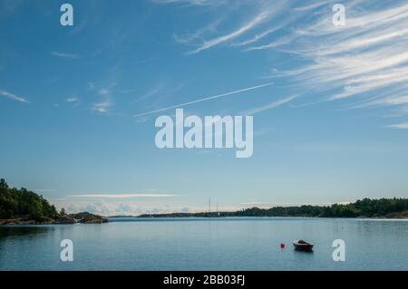 Eine ruhige Sommermorgend-Szene mit einem Boot auf dem Stillwasser zwischen den Inseln im Archipel von Kragerø, Skåtøy, Südnorwegen. Stockfoto