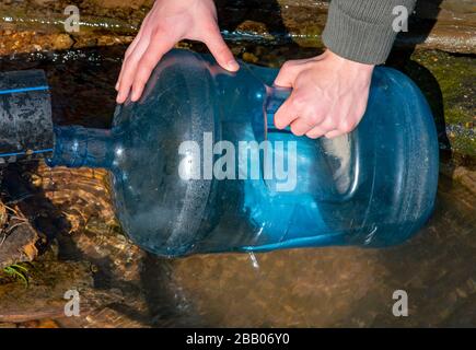 Die Hände der Männer füllen eine Plastikflasche mit Wasser aus einer Feder. Stockfoto