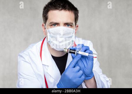 Der junge Arzt in einer Schutzmaske und Handschuhe hält einen Coronavirus-Test in seinen Händen Stockfoto