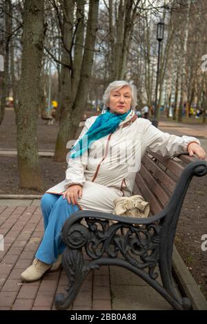 Eine elegante ältere grauhaarige Frau sitzt auf einer Parkbank. Stockfoto