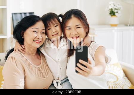 Fröhliche junge Asiatin, die selfie mit ihrer Tochter und ihrer älteren Mutter nimmt Stockfoto