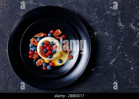 Gekochte weiche brie mit Pekannuss, Blaubeeren, Preiselbeeren und Honig auf einem schwarzen Teller auf dunklem Betongrund, horizontaler Ansicht, c Stockfoto