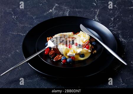 Weihnachts-Vorspeise-Ahorn-Pekan gebackenen brie-käse mit Beeren: Blaubeeren, Preiselbeeren und Honig oben auf schwarzem Teller mit silberfarbenem Besteck serviert Stockfoto