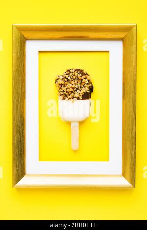 Dessert als Art Brownie-Kuchen in Form von Popsicle in goldenem Rahmen auf gelbem Hintergrund. Stockfoto