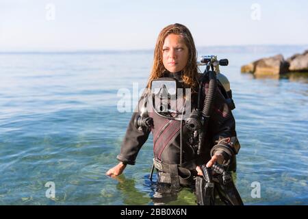 Tauchlehrer für Frauen, die in Wasser stehen und einen Trockenanzug, einen Doppeltank und Halteflossen tragen Stockfoto