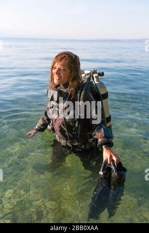 Tauchlehrer für Frauen, die in Wasser stehen und einen Trockenanzug, einen Doppeltank und Halteflossen tragen Stockfoto