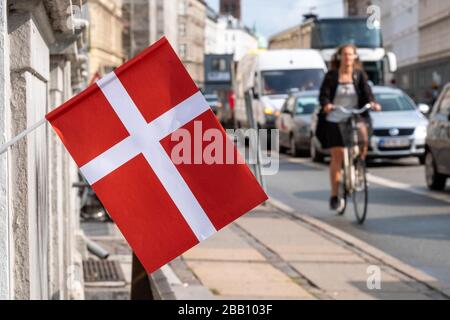 Frau, die mit ihrem Fahrrad an einer dänischen Flagge in den Straßen von Kopenhagen, Dänemark, Europa vorbeifährt Stockfoto