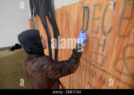 Der Graffiti-Künstler Olivier Roubieu wendet den letzten Schliff auf sein Wandbild an, das Sandown's Tingle Creek Christmas Festival während des Gentleman's Day wirbt Stockfoto