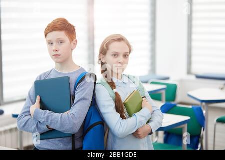 Taille oben Porträt von rothaarigen Teenager-Jungen und Mädchen, die sich zurücklehnen, während sie in der Schule posieren und Bücher halten, kopiere Raum Stockfoto