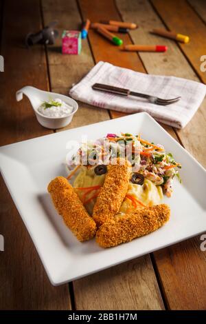 Kinder essen Fischfinger mit Kartoffelpüree und gemischtem Salat Stockfoto