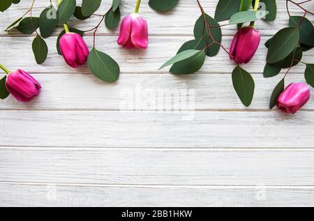 Wunderschöner Blumenstrauß aus rosafarbenen Tulpen mit Eukalyptus auf weißem Holzhintergrund. Draufsicht, flacher Lay. Stockfoto