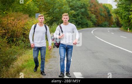 Freunde, die hitchhitchhamps unterwegs Beginnen Sie mit dem Wandern ein tolles Abenteuer in Ihrem Leben. Firmenfreunde Reisende, die auf dem Naturhintergrund der Straße hitchwandern. Fahren Sie in der Nähe des Stadtrandes. Reisende auf dem Weg. Stockfoto