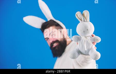 Lustiger Hünenmann mit Bart und Schnurrbart. Konzept des Ostersymbols. Kerl bärtiger Flusspferd süßer sanfter, bunter langer Ohren blauer Hintergrund. Osterhase. Respekt vor Traditionen. Mann trägt einen kuscheligen Plüschanzug. Stockfoto