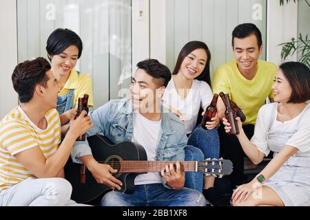 Positive Freunde klinken Flaschen Bier, wenn ihr Freund Gitarre spielt und für sie singt Stockfoto