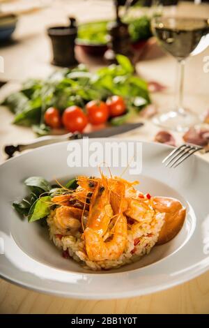 Nahaufnahme von Meeresfrüchten gebratene Garnelen mit Risotto auf weißem Teller Weißwein und Tomate im Hintergrund Stockfoto