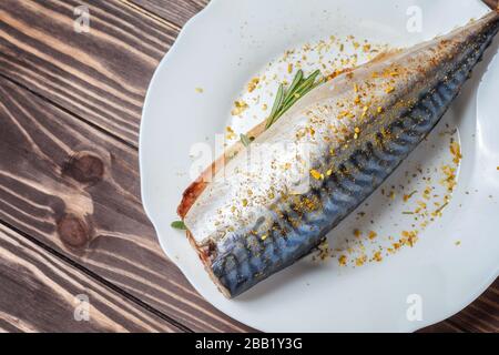 Eingepickte Makrele in einer weißen Platte. Roher, nicht zubereiteter Fisch. Traditionelle Fischspezialität, gesundes Esskonzept. Vor dem Hintergrund einer Holztischplatte Stockfoto