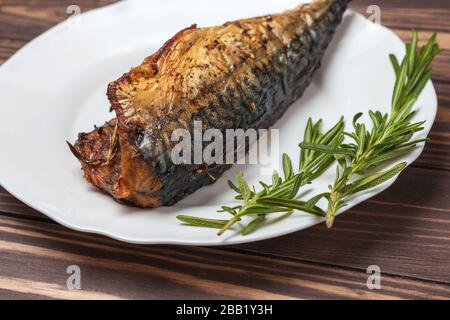 Gebratene Makrele mit Rosmarin. In einer weißen Platte auf einer Holzunterseite. Nahaufnahme Stockfoto