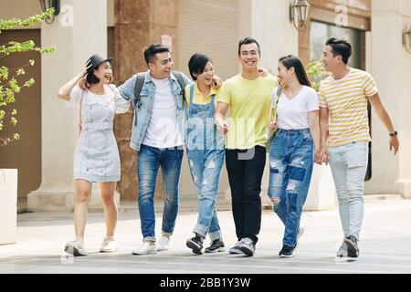Lachend umarmende vietnamesische Gruppe von Studenten, die auf der Straße spazieren gehen Stockfoto