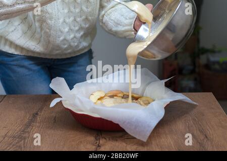 Die Hostess bereitet apple charlotte zu Hause in der Küche zu und gießt den Teig zu einer Backform. Roher Apfelteig Stockfoto