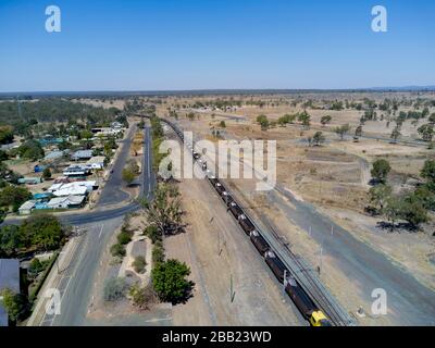 Antenne mit 120 Wagen und 2 km langem Güterzug, der den Export zum Hafen von Gladstone befördert, während er durch das Dorf Dingo Central Queensland führt Stockfoto
