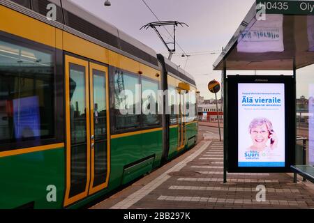 Helsinki, Finnland. März 2020. Straßenbahn HSL in Fahrt mit Abfahrt Olympia Terminal Tram Haltestelle für nur 3-4 Personen (nicht auf Foto) an einem Montagmorgen. Die Meldung des finnischen Instituts für Gesundheit und Wohlfahrt zum Ausbruch des Coronavirus wird auf dem Bildschirm angezeigt. Stockfoto