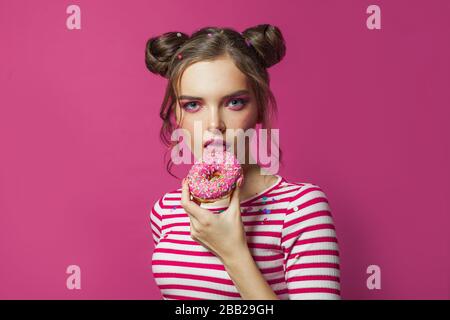 Süß lustig. Hübsche Frau leckt Donut auf lebhaftem rosa Hintergrund Stockfoto