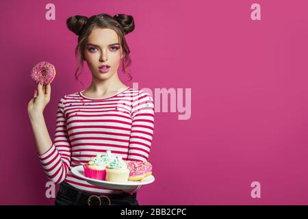 Hübsche Modelfrau mit Dessertbonbons und Snacks auf lebhaftem pinkfarbenem Hintergrund Stockfoto