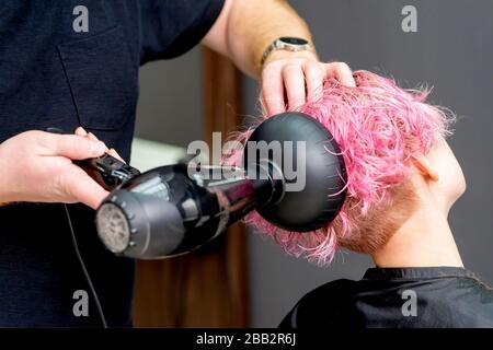 Die Hände des Friseursalons trocknet die rosafarbenen Haare der Frau aus der Nähe. Stockfoto