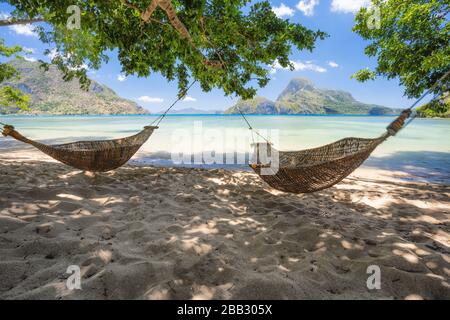 El Nido, Palawan, Philippinen. Bambus Hängematten am Ufer im Schatten. Schöne tropische Lagune mit epischer Cadlao-Insel im Hintergrund Stockfoto