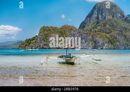 Palawan, Philippinen. Traditionelles filippino banca Boot in der flachen blauen tropischen Lagune in der Bucht von El Nido. Kalksteingebirge von Cadlao Island in Stockfoto