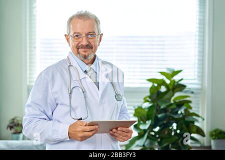 Medizinische leitender Arzt mit einem Stethoskop. Auf einem blauen Hintergrund. Ein medic hält eine Tablette in der Hand und macht einen Termin mit der Klinik. Krankheit Stockfoto