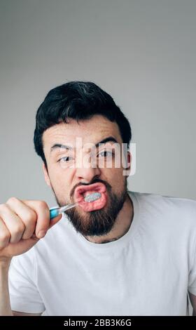 Junger Mann isoliert über Hintergrund. Kerl, der seine Zähne stark und konzentriert säubert. Mit Zahnbürste und Zahnpasta für die Gesundheit sorgen. Schauen Sie auf die Kamera Stockfoto