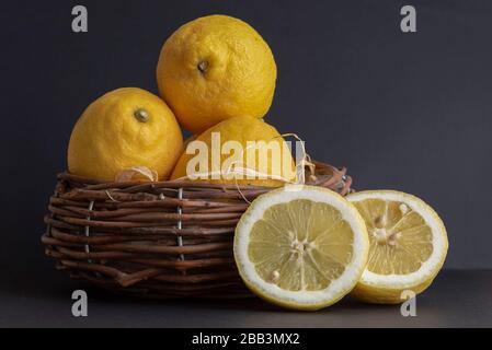 Stillleben mit frischen Sorrento Zitronen und frischen Zitronenscheiben in einem Strohkorb auf einem Tisch Stockfoto