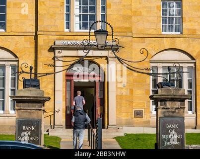 Haddington, East Lothian, Schottland, Großbritannien. März 2020. Covid-19 Coronavirus lockdown wirkt sich auf die normalerweise belebte Marktstadt an einem schönen Frühlingstag mit leeren Straßen und sozialen Distanzierungen der Menschen aus. Die Leute warten außerhalb einer Bank of Scotland Filiale 2 Meter voneinander entfernt Stockfoto